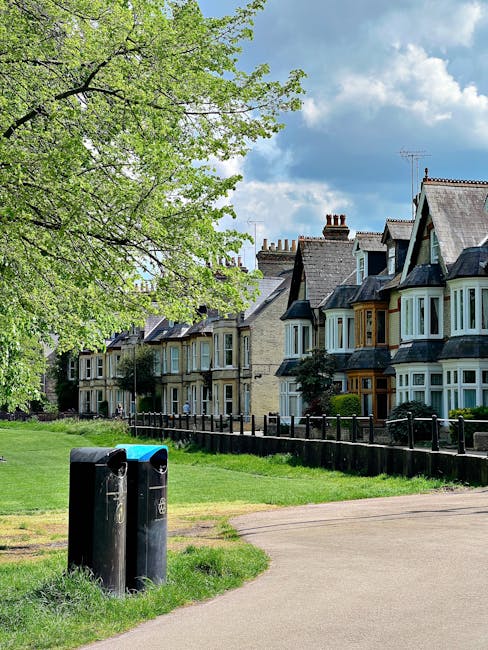 A row of old-fashioned terraced houses with bay windows and slate roofs, situated along a quiet residential street. In the foreground, two black waste bins with slightly weathered surfaces are positio