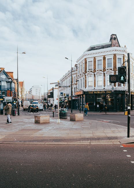 A wide view of a busy high street intersection featuring a historic, three-storey building with a corner shopfront displaying the sign 'The World's End' on the ground floor. The building has a white f